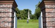 Image is of open gates leading to a monument in the gardens. There is a couple walking towards the gates.