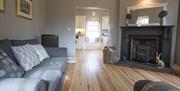 Image shows lounge area with wooden floor, sofa, fireplace with wood burner and open plan through to kitchen