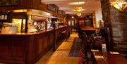 A wooden bar area with set tables, barstools and seating booths.