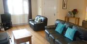 Image shows lounge area with leather sofa and chair, coffee table and TV