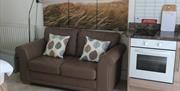 A kitchen with a cooker and a brown sofa under a photo of a beach.