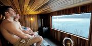 Three people in a sauna overlooking the lake