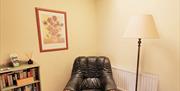 Image shows the reading nook with large armchair, shelf of books and small round side table and floor standing lamp.