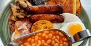 Plate of a traditional Irish fry featuring soda bread, potato bread, sausages, crispy bacon, black pudding, baked beans, sautéed mushrooms, a sunny-si
