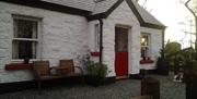 Outside view of cottage with red door and wooden chairs at front