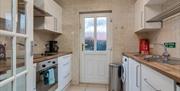 A photo of a kitchen with an oven, sink, washing machine, bin and a back door.