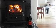 Closeup of wood burning in a fireplace with a wine bottle and a view into the kitchen.