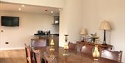 Image shows dining table and chairs, wooden floor and TV on wall