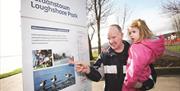 A man and child looking at pictures on the park's information board.