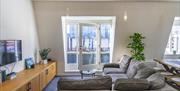 A living room with a large corner sofa, a TV, a glass balcony door and an indoor plant.