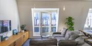 A living room with a large corner sofa, a TV, a glass balcony door and an indoor plant.