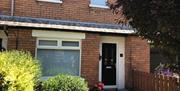 A photo of the front of a house with a black front door and bushes in the garden.