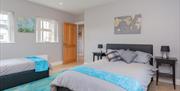 A large bedroom with a single and double beds, bedside tables, windows and paintings.