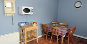 Image shows kitchen area with dining table and 5 chairs, microwave on wall with small table underneath