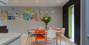 An orange dining room table with orange and white chairs, flowers and pencil style art of Belfast.