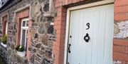 Image shows front door of property with flower beds on window sills