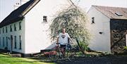 Image shows man standing in a garden with a bicycle outside property