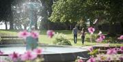 Image is of the Wallace Fountain and flowers in the foreground with a couple walking hand in hand in the background