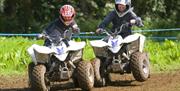 Image is of 2 children on mini quad bikes