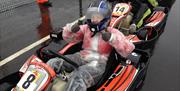 A girl in a waterproof racing suit and helmet giving a thumbs-up.