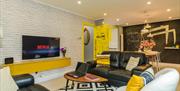 An open plan sitting room with sofas, a chair, a coffee table and a tv which leads to a dining room.