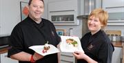 Two teacher chefs smiling and holding plates of food.