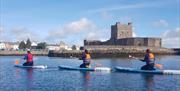 image of 3  paddleboarders kneeling on boards in water in front of Carrickfergus Castle.