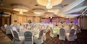 A photo of a large function room with tables set and decorated for a wedding.