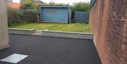 Back garden with a large blue shed and a gardener tending to a raised lawn.