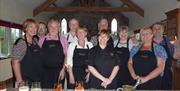 A class of cookery students smiling with desserts they have made.