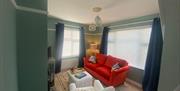 Living room with bright orange velvet sofa, white armchair and colourful rug