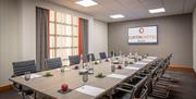 A meeting room with a TV and a conference table set with water, paper and apples.