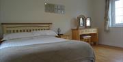 Image shows double bed in room with wooden floor and beside table, dressing table and window