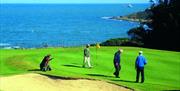 Photo of golfers in play on the green with waters of Belfast Lough in background