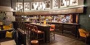 A photo of bartenders working behind a curved bar and a high table surrounded by bar stools.