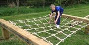 A boy climbs a net on the low ropes course.