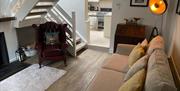 Image shows lounge with sofa and armchair, wood floor and view of stairs and kitchen