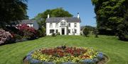 A house at the end of a lawn with a large circular flowerbed.