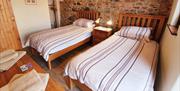 Image shows twin bedroom with dressing table. 1 small window and 1 larger window. Feature wall with exposed stonework.