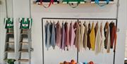Interior of Bramble Green studio: railings holding a variety of colourful knitted jumpers and a table with knitted hats