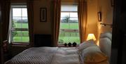 A double bedroom with two windows looking out at the countryside.