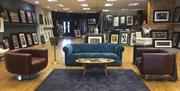 Photo of the inside of the gallery showing seating area and paintings on display for sale