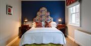 Image shows double bed with bedside tables and lamps plus radiator and window