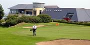 Photo of Club house and a golfer on the green to the forefront