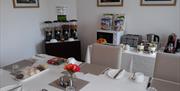 Dining room set for breakfast with tea/coffee making supplies, a toaster, a microwave, fruit and a selection of cereals.