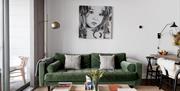 A living room with a green sofa between a dining room table and balcony doors.