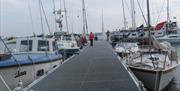 Image shows a walkway and various types of boats in a marina