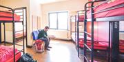 A photo of a man sitting in a large room with three bunk beds.