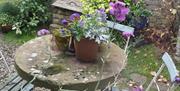 Image shows round stone table and 3 blue chairs in courtyard.