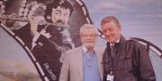 Two men standing in front of a mural of Sir James Galway.